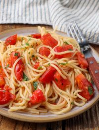 A vertically aligned photo of a plate of tomato pasta on a wooden tabletop.