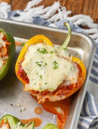 A stuffed pepper with a cheesy topping is visible on a metal baking sheet in this vertically aligned photo.