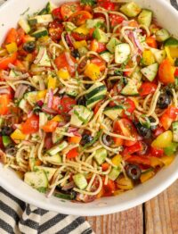 marinated pasta salad with vegetables in white mixing bowl on wooden table