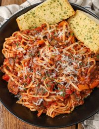 spaghetti with mushroom marinara sauce on black plate with garlic bread