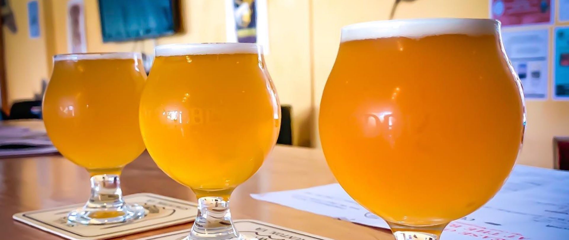 Three glasses of local craft beer rest on coasters and a patron table. 