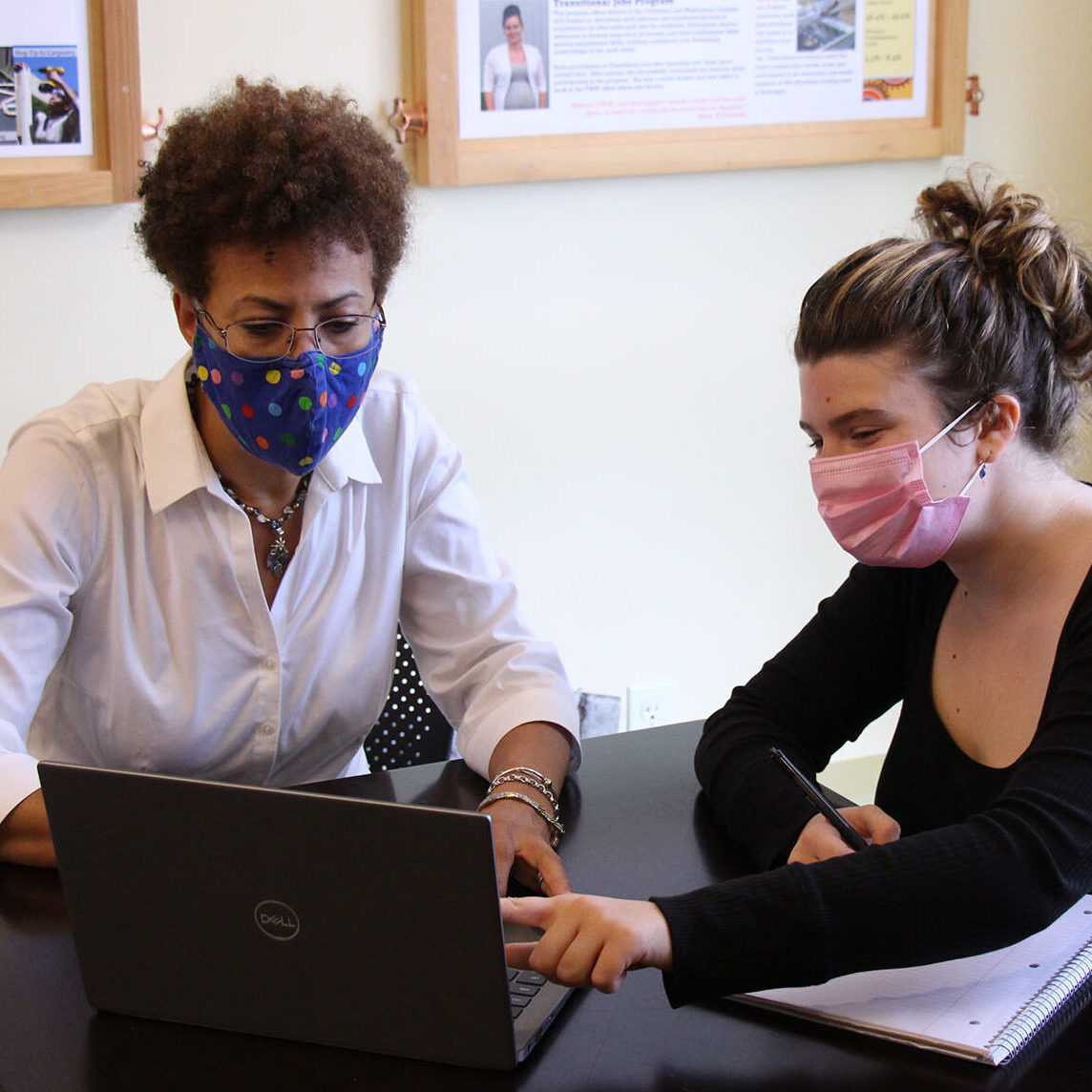 Past VWW intern working with VWW staff member on a laptop for employment and career services. Vermont Works for Women offers internships in communications and marketing, fundraising, and programming.