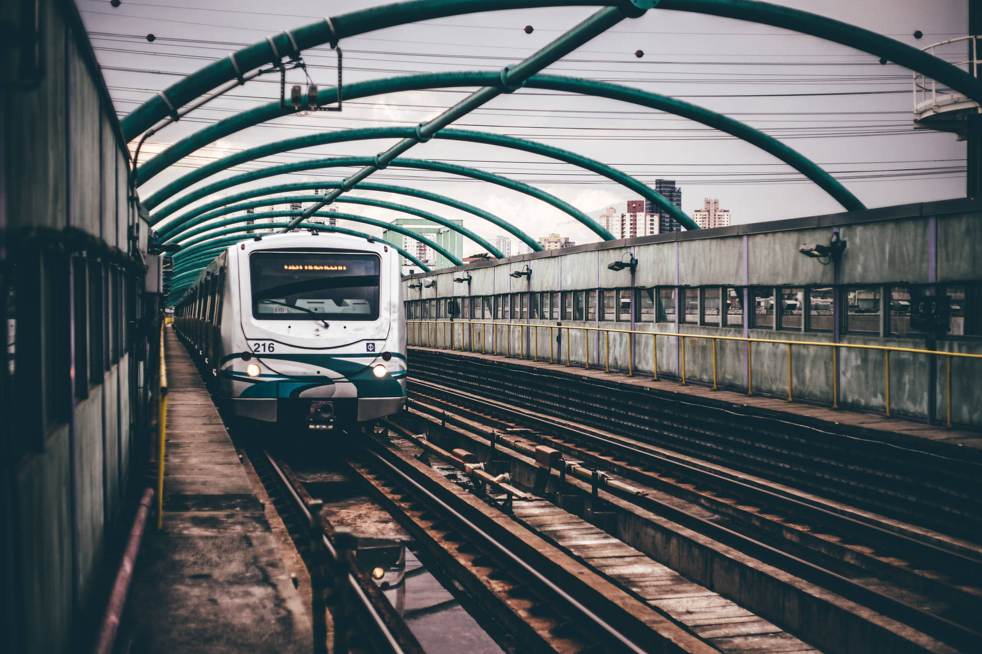 A lonely white train pauses at a gloomy station on a drizzly day Wallpaper