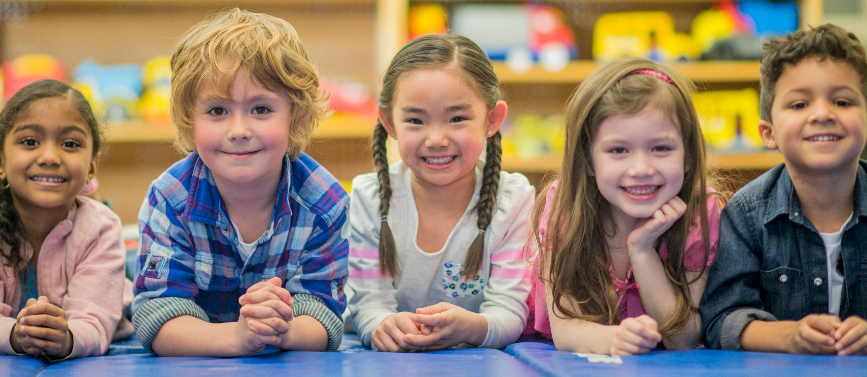 A group of diverse young children sitting at a table facing and smiling at the camera.