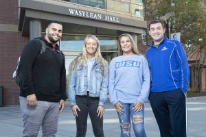 A group of 4 Worcester State students standing in front of Wasylean Hall on campus