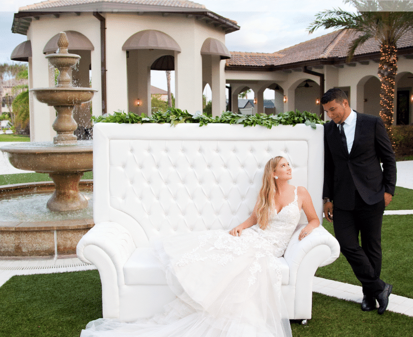 Oasis Club at ChampionsGate - bride on upholstered couch near outdoor fountain gazing at husband