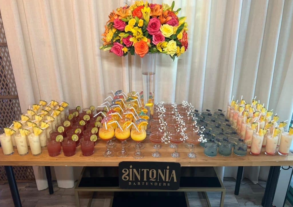 display of six different cocktails on a table, with a large tall floral display that compliments the drinks, SINTONIA BARTENDERS, Orlando, FL