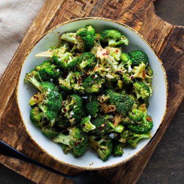 Square overhead photo of marinated broccoli in a bowl sitting on a wooden cutting board.