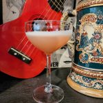 A Commodore Cocktail in a coupe glass sitting in front of a ukulele.