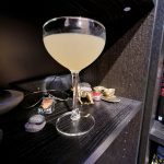 A Margarita sitting on a book shelf with assorted items.