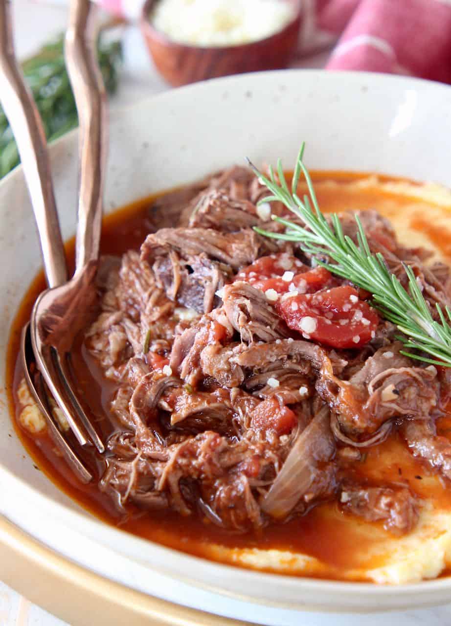 Shredded beef ragu in bowl served over polenta with fresh rosemary