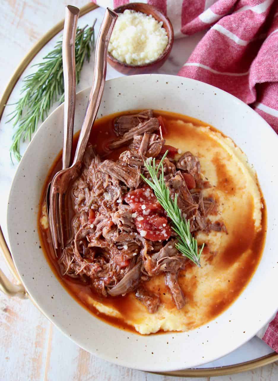 Slow cooker shredded beef ragu in bowl with creamy polenta