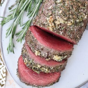 sliced beef tenderloin on a plate with fresh rosemary