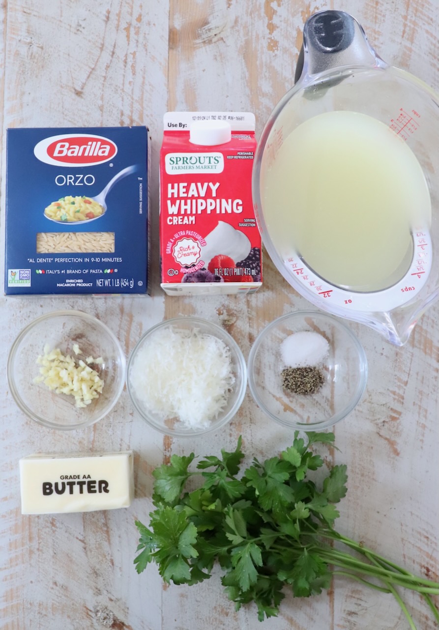 ingredients for creamy orzo pasta on a white wood board