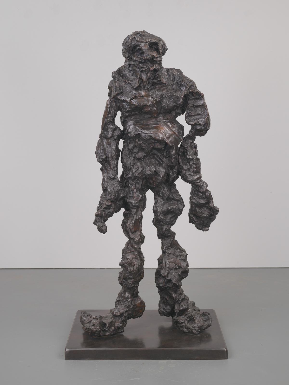 A bronze sculpture of a humanoid figure with a textured, rough surface, standing on a rectangular base against a plain background. The figure appears dynamic and organic, with an emphasis on form and texture over fine detail.