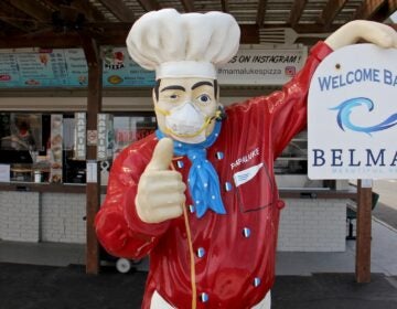 A figure in front of Mamalukes Pizza on Ocean Avenue in Belmar wears a protective mask. (Emma Lee/WHYY)