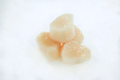 Four raw scallop pieces on a white background.