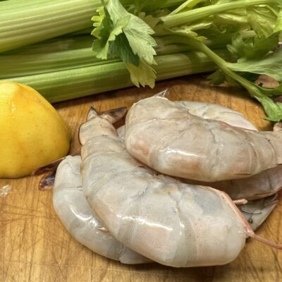 Raw shrimp, lemon, and celery on a cutting board.