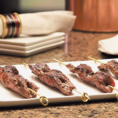 meat skewers on a plate on a table with a candle on the side