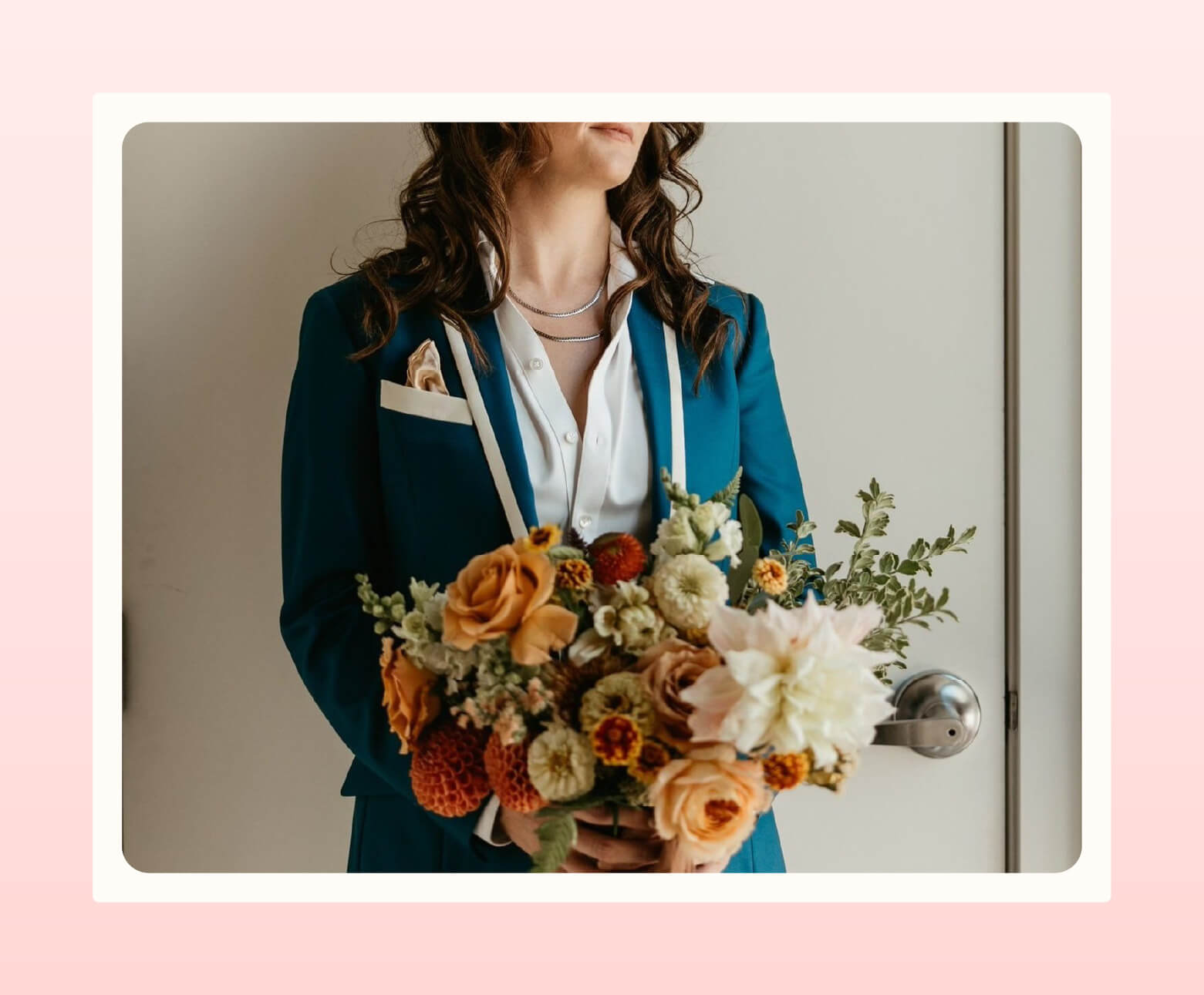 A person wearing a tailored blue suit with white accents from Duchess Clothier stands holding a bouquet of orange and cream flowers