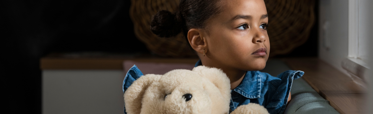 Child with teddy bear looks out window