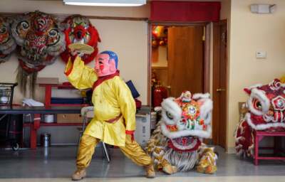 A Buddha introduces a lion to the stage in a parade rehearsal at the Boston Wong Family Benevolent Association practice room. (Cici Yu/WBUR)