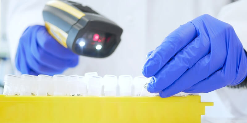 A lab technician in blue gloves scans vials of chromatography consumables with a barcode scanner in a modern laboratory.