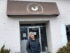 A person stands in front of a building. An awning above her says Ithaca Coffee Company with a rooster logo.