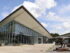 An exterior of an angular museum building with metal and glass, and a sculpture of a dinosaur in front