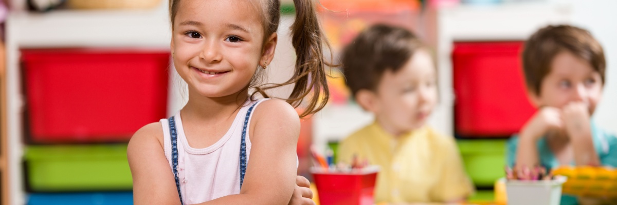 Young child sitting in a classroom smiling.