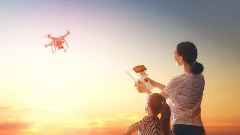 Little girl and her mother are operating the drone by remote control in the park. Kid and mom are playing with quadrocopter outdoors.