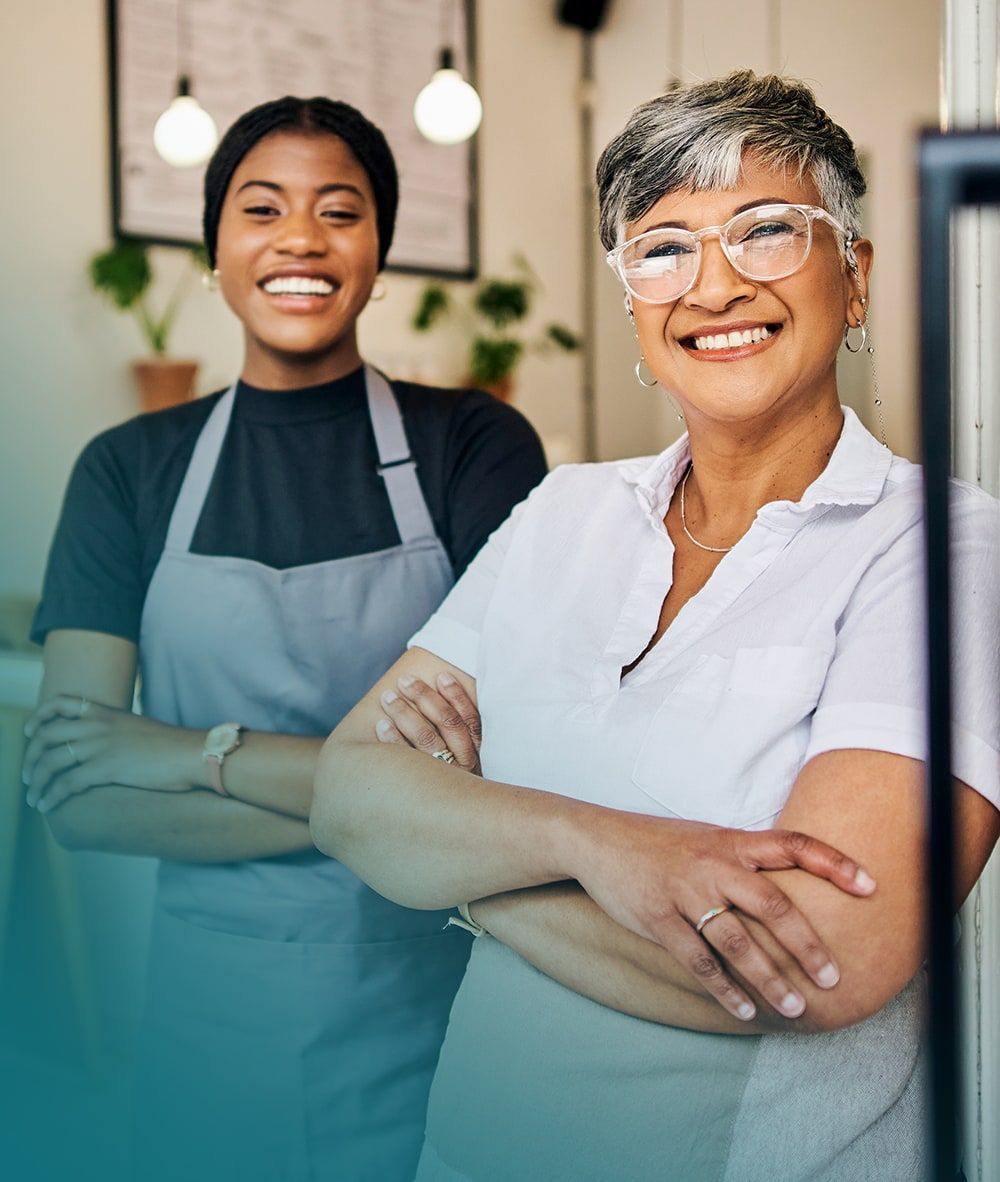 Deux employées souriantes les bras croisés, dont une porte un tablier