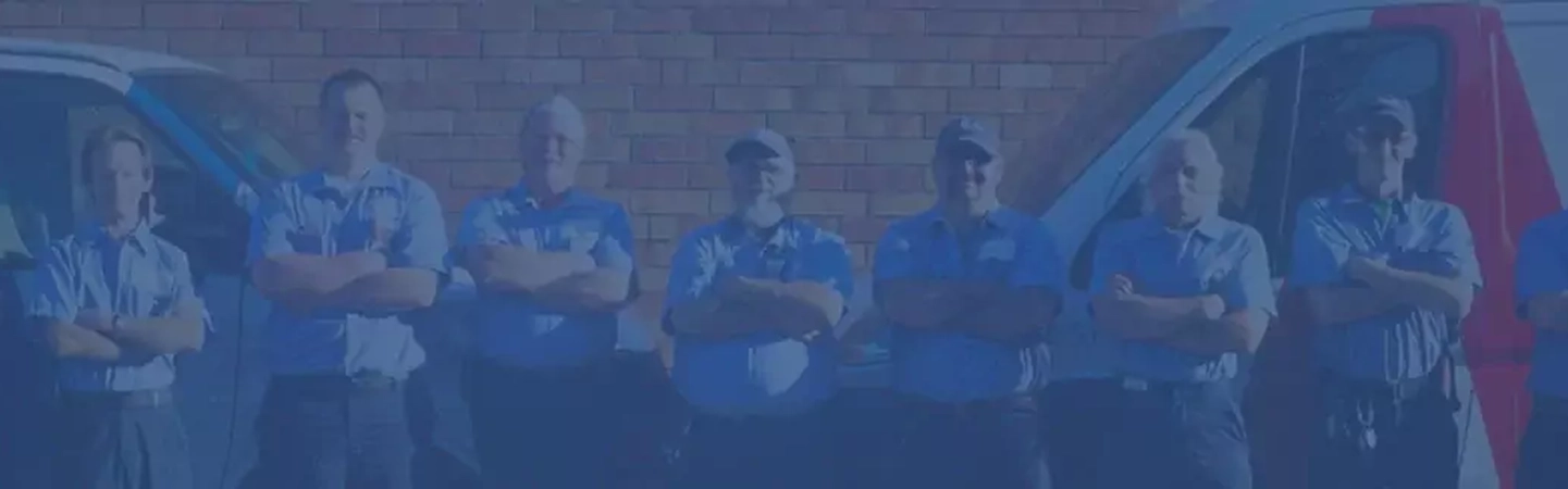 Row of Aire Serv technicians standing with arms crossed between pair of branded vans. 