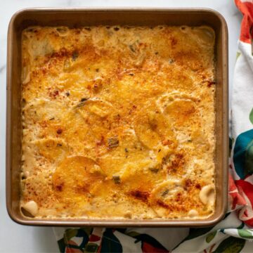 A golden-brown scalloped eddoe dish baked in a square pan, topped with spices, resting on a colorful floral kitchen towel.