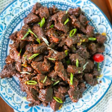 Serving dish of Guyanese casareep lamb with scallions as garnish.