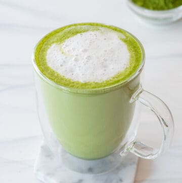 coconut matcha latte in clear mug sitting on marble coaster on gray background