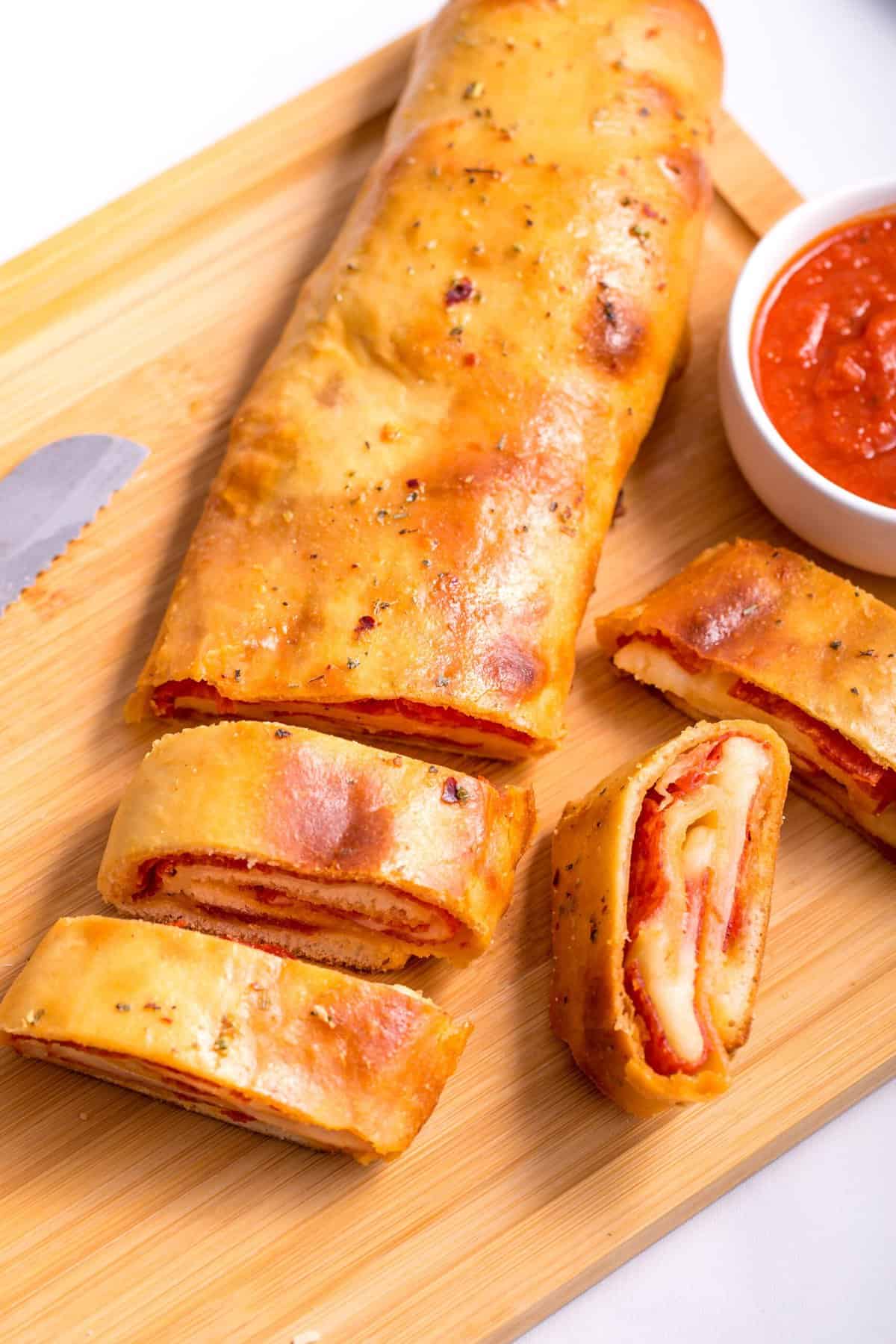 sliced pepperoni bread served on a wooden board with a side of pizza sauce