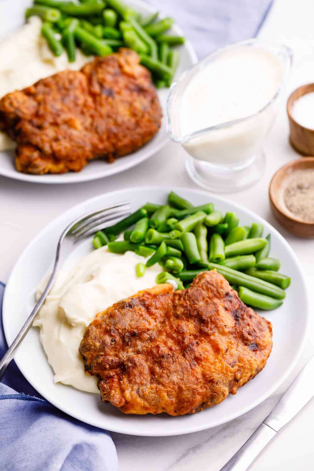 plate of air fryer chicken-fried steak served on a white round plate with a side of mashed potatoes and green beans.