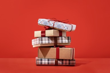 Several buff and checked gift boxes with red bow in pile on red background, side view. Holiday