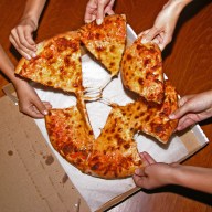 People grabbing slices of pizza, overhead view