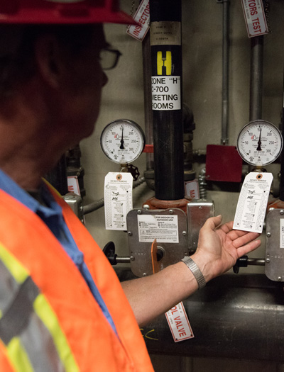 Two coworkers wearing hard hats and safety gear discuss the status of a unit while looking at a handheld computer.