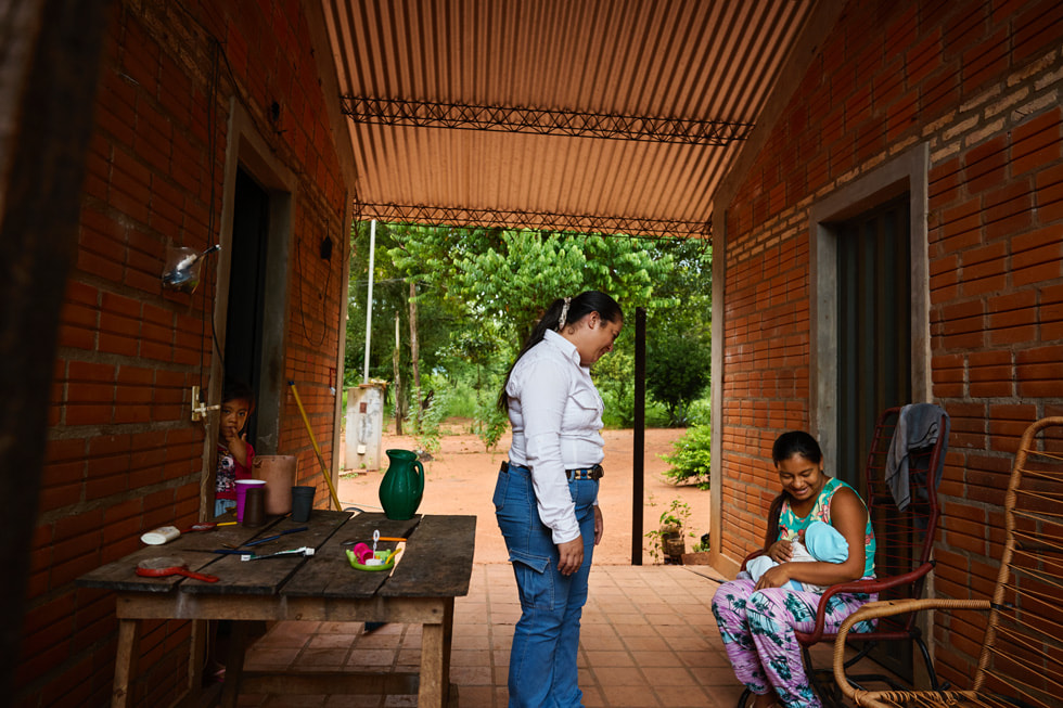 Gladys Nuñez stands in a walkway facing a person holding a baby as a child looks on from a doorway.