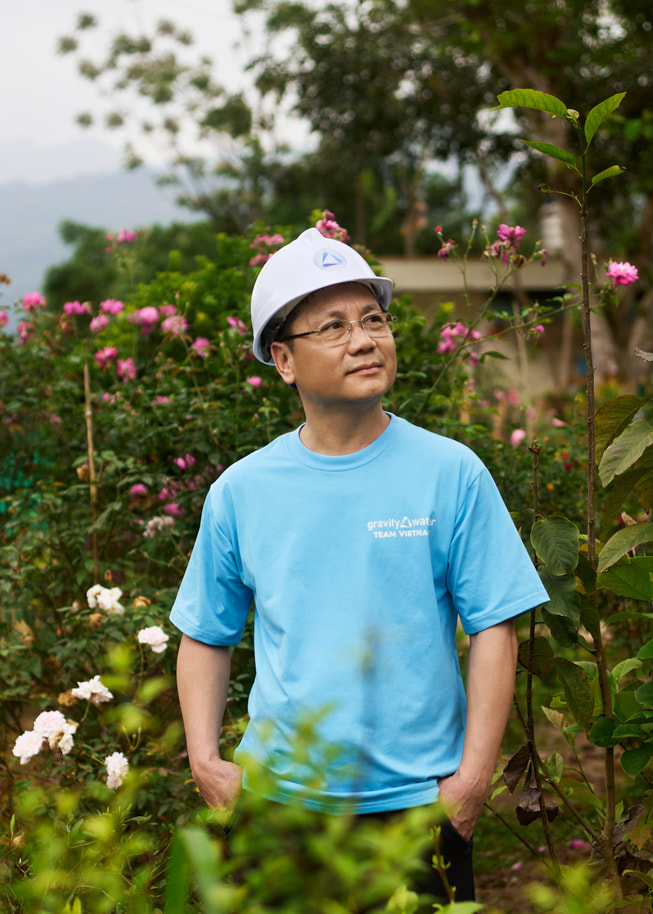 Et portræt af Phan Viet Dung, som står udenfor med en sikkerhedshjelm på hovedet og blomster i baggrunden.