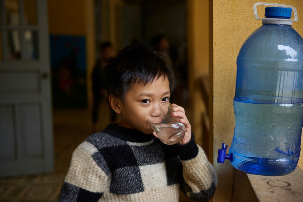 Billedet viser en elev, der drikker vand fra Gravity Water-systemet på Vay Nua Primary and Secondary Boarding School for etniske minoriteter.