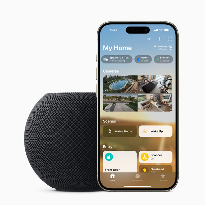 HomePod mini สีมิดไนท์ตั้งอยู่ข้าง iPhone 15 Pro ที่แสดงเมนูบ้านของฉันต่อผู้ใช้งาน