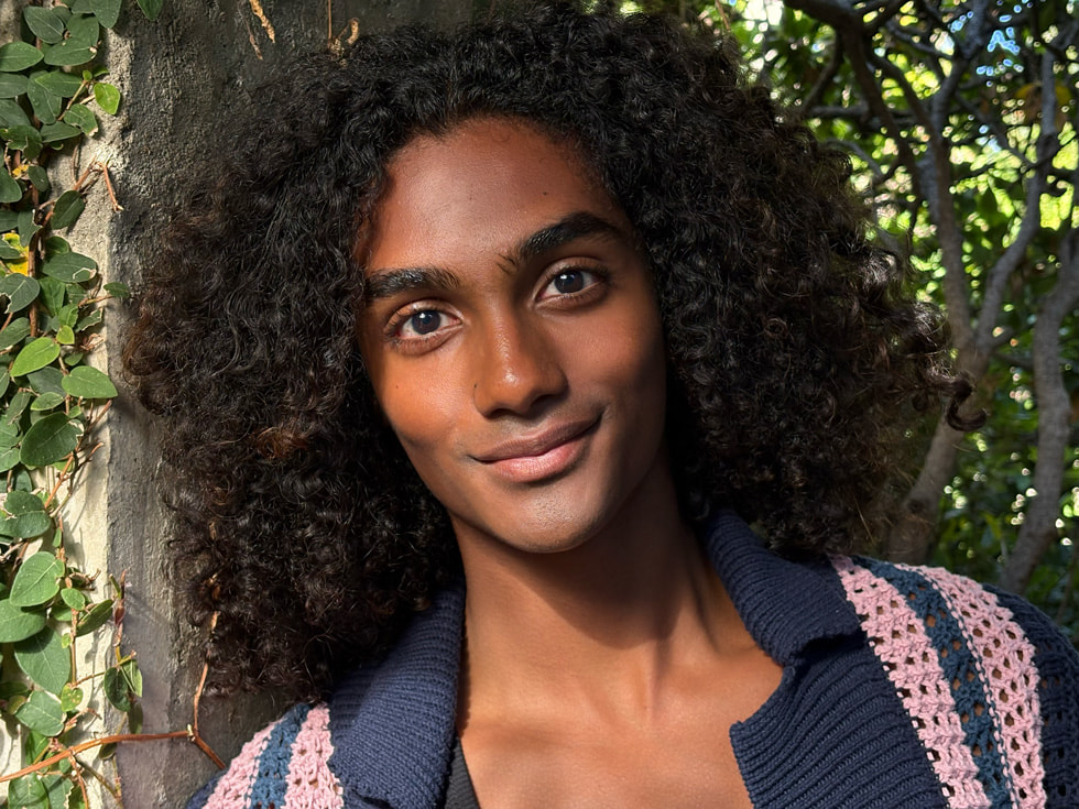 The same headshot shown in the previous image — with a person and foliage in the background — is now zoomed in.