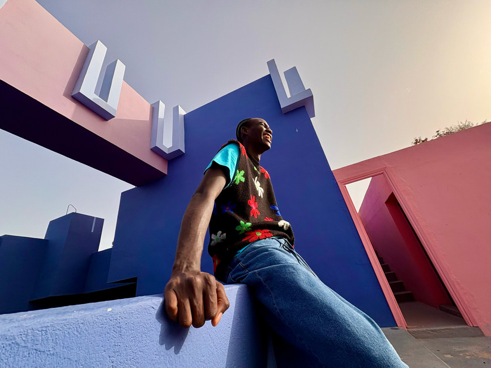 An image of a person leaning on a colorful pink-and-purple building. 