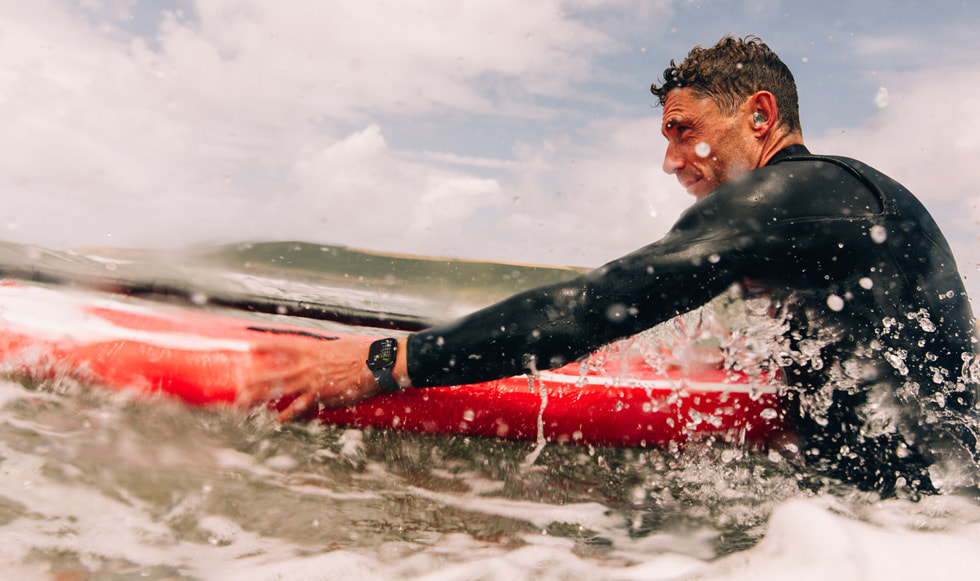 A surfer wears Apple Watch Series 10 while navigating whitewater out in the ocean.