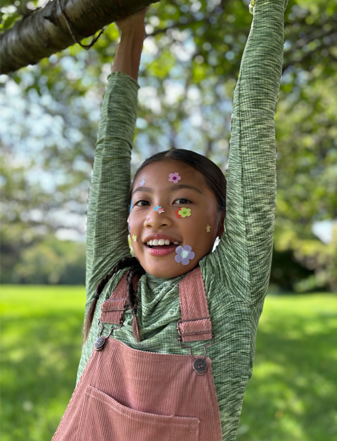 Close-up photo of a girl with flower stickers on her face taken with the iPhone 2x optical-quality Telephoto on iPhone 15