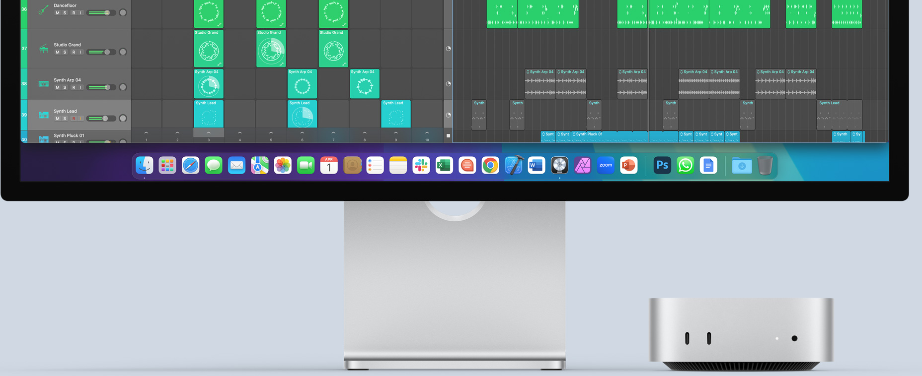 Front of silver Mac mini showing front ports and indicator light, fitting underneath a Mac monitor showing a colorful screen and app icons in the Dock